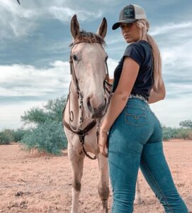 Tall Blonde woman stands next to a horse