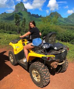 A pretty girl rides a yellow ATV quad in a jungle.